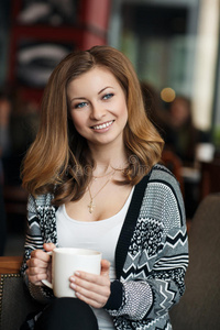 美丽的年轻微笑的女人在咖啡馆喝咖啡