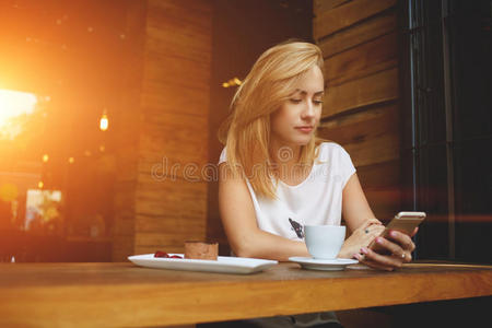 漂亮的时髦女孩在咖啡馆早上早餐时在手机上看视频
