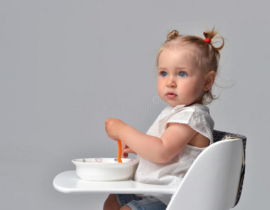 儿童蹒跚学步的孩子坐在白色婴儿椅子桌子上，拿着盘子和勺子
