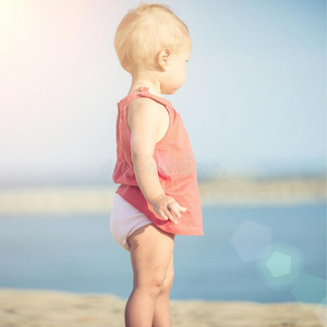 穿着红色连衣裙的女婴在海边的沙滩上玩耍。