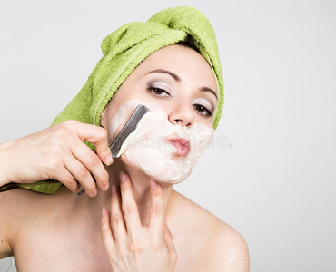 护肤行业漂亮的年轻女人穿着浴巾,用直剃刀刮胡子.