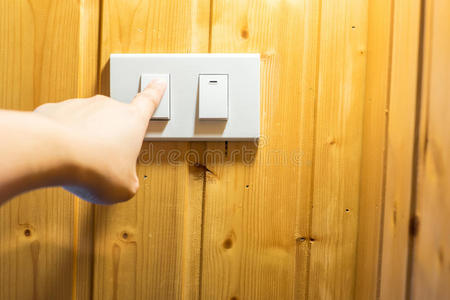 手指按下木墙上的灯开关按钮照片