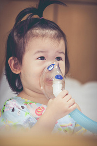 亚洲儿童持有用于治疗哮喘的面罩蒸气吸入器。