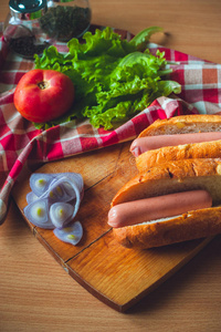 面包与香肠热狗，紫色洋葱，一个西红柿和沙拉。 木板上的膳食成分