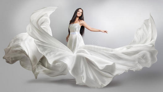 穿着白色飞裙的漂亮女孩。 流动的织物。 轻盈的白布飞舞