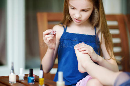 可爱的小女孩在家里玩得很开心，用五颜六色的指甲油做指甲和涂指甲