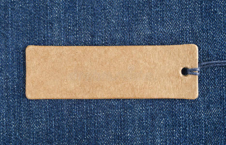 蓝色牛仔布上的空白纸标签. 牛仔裤背景与销售或价格标签.照片
