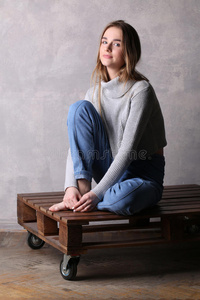 甲板脖子膝盖弯曲的女孩坐在甲板上. 灰色背景照片