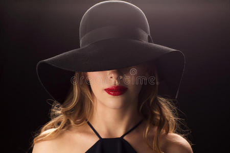 戴黑帽子的漂亮女人在黑暗的背景下