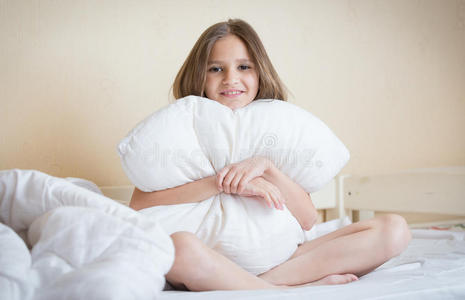 美丽的黑发女孩坐在床上拥抱白色枕头