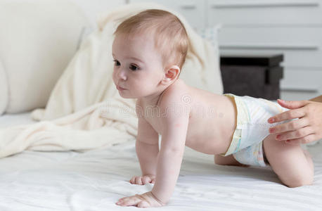 9个月大的婴儿，穿着尿布，爬在床上，铺着白色的床单