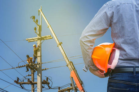 电气工程师手持安全帽，电工用起重机在电力杆上工作