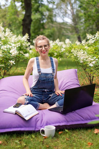 在花园工作的自由职业者。 写作，上网。 年轻的女人在公园区放松和玩得开心