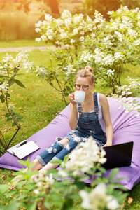 在花园工作的自由职业者。 写作，上网。 年轻的女人在公园区放松和玩得开心