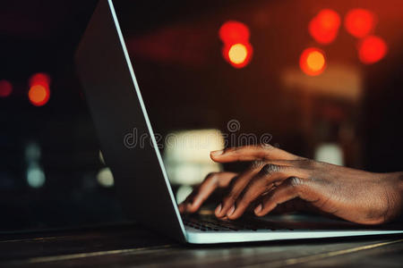 黑人的手在键盘上打字。 使用笔记本电脑的人。 美丽的灯光作为背景。 色调