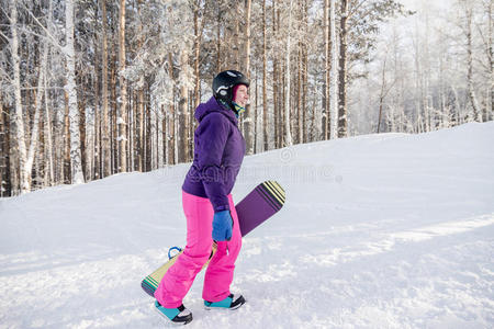 穿着紫色夹克和粉红色裤子的女孩手里拿着滑雪板