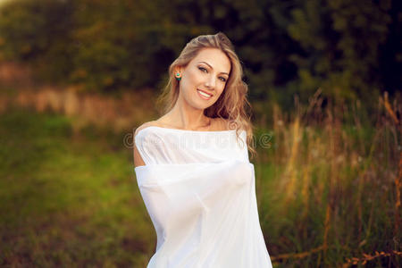 美丽快乐的年轻女人，长发站在傍晚的阳光下，转向白色的毯子和微笑的乐趣