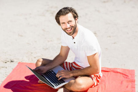 在海滩上使用笔记本电脑的男人