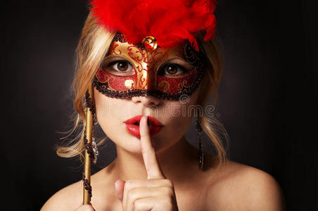 带着狂欢节面具的女孩。 女人用手指在她的红嘴唇上，露出沉默