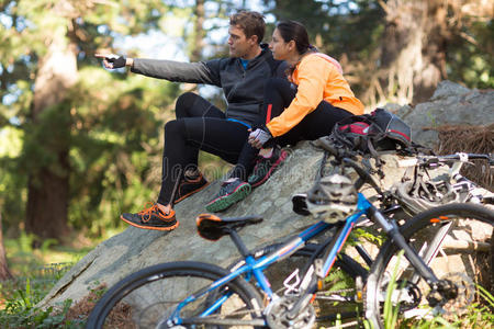 骑自行车的夫妇坐在岩石上，指着远处的森林