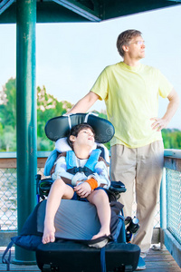 父亲坐在湖边，残疾的儿子坐在轮椅上