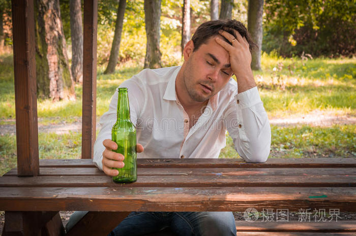 醉汉坐在长凳上拿着啤酒瓶