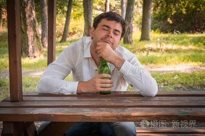 醉汉坐在长凳上拿着啤酒瓶