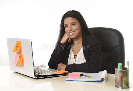 有吸引力的西班牙裔女商人坐在办公桌上，在电脑笔记本电脑上工作，微笑着快乐