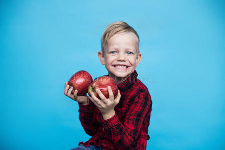 英俊的小男孩带着两个红色的苹果。 蓝色背景的工作室肖像