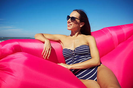 一个可爱的女人坐在海滩上的粉红色充气船上