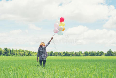 年轻的时髦的亚洲女人的背部，在草地上有彩色气球