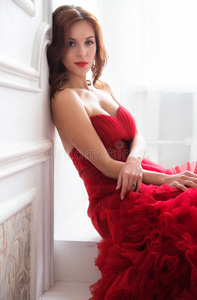 美丽的黑发模特女人穿着晚红礼服。 美丽时尚，豪华化妆和发型