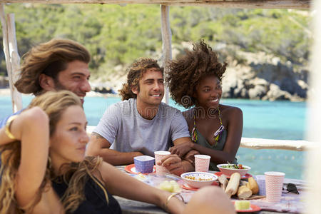 四个朋友在海边的一张桌子上交谈，西班牙伊比萨