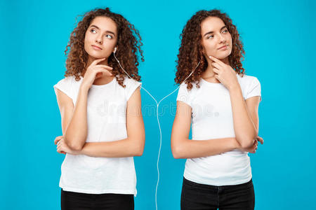 女孩们双胞胎在耳机里听音乐，在蓝色背景上思考。