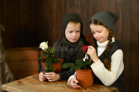一个男孩和一个穿着老式连衣裙的女孩坐在一张旧桌子上。 看着花