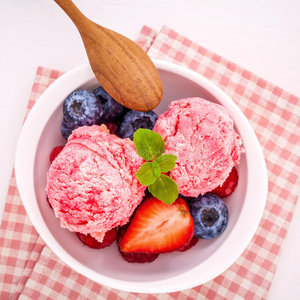 关闭冰淇淋混合浆果水果，覆盆子，蓝莓，草莓和薄荷叶设置在白色碗白色木制