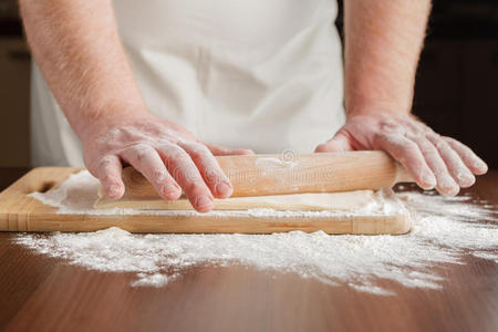 面包师把面团擀在洒了wi的木制厨房桌子上