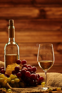一瓶白酒,玻璃和葡萄放在木制内部的袋子上照片