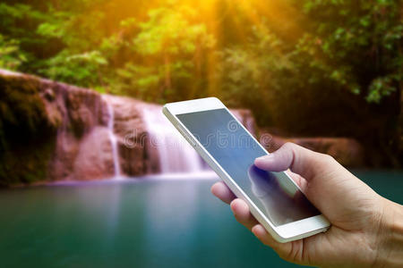 手持智能手机在模糊的背景泰国瀑布