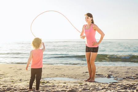 家庭锻炼母亲和女儿在海滩上做运动。