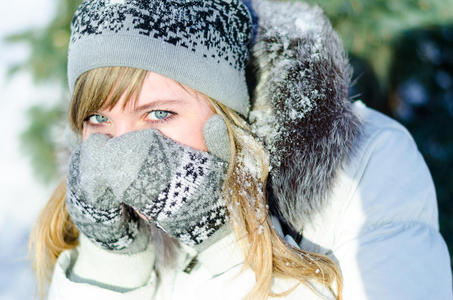 戴着帽子和手套的漂亮金发女孩在寒冷中遮住了他的脸照片