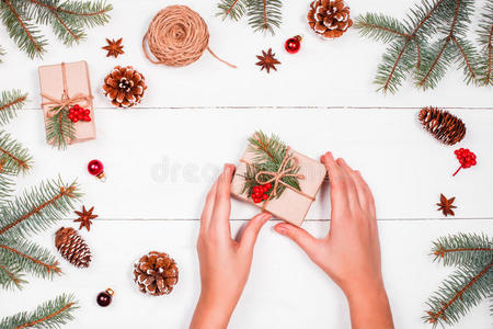 圣诞背景有冷杉枝，松果，黄麻，红色装饰品。 女性手拿着圣诞礼物。 圣诞节和