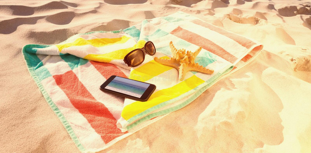 海星与太阳镜和手机的复合图像保存在海滩毯子上