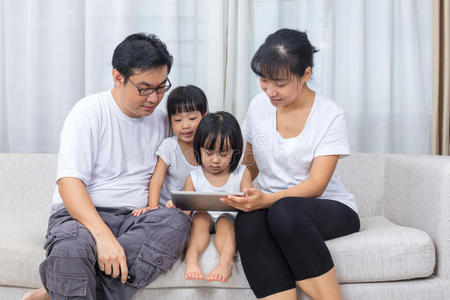 亚洲的中国父母和女儿在沙发上使用平板电脑