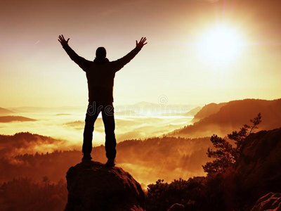 秋天朦胧的早晨在大自然中. 黑衣徒步旅行者站在岩石的顶峰上照片