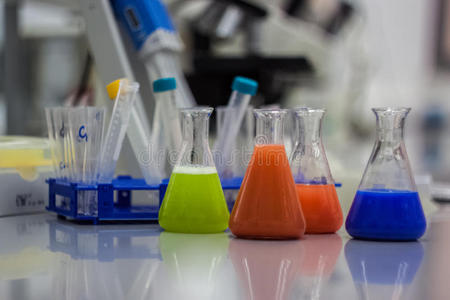 用于研究的生物技术实验室设备。 烧瓶，瓶子和吸管与彩色橙色，绿色和蓝色液体和