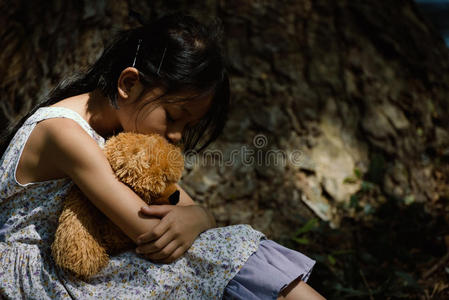 在坏的可爱的小女孩可爱的悲伤女孩和泰迪熊在公园,小女孩正在拥抱一