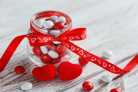 五颜六色的糖果罐装饰着红色的蝴蝶结，白色的木制背景上有心形。 情人节概念