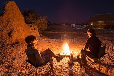 一对夫妇晚上坐在燃烧的篝火旁。 在沙漠里露营，背景是野生大象。 夏季冒险和E