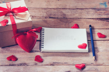 空白笔记本和礼品盒，红色的心在木材背景上。